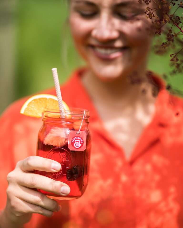 A happy woman holding a refreshing iced tea from Teekanne in summer.